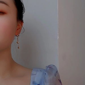 Gros plan de boucles d'oreilles créoles cœur dorées avec pompons portées sur l'oreille