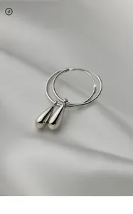 Gros plan de boucles d'oreilles créoles goutte d'argent sur fond de satin blanc