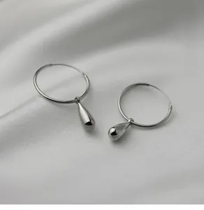 Détail de boucles d'oreilles créoles goutte d'argent sur tissu en soie blanche douce