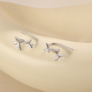 Close-up of S925 sterling silver butterfly drop earrings on a minimalist cream stand