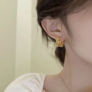 Détail rapproché de boucles d'oreilles dorées en forme de C au design plissé