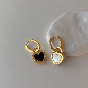 Détail de boucles d'oreilles cœur avec incrustation de nacre noire et blanche et bords dorés