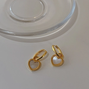 Gros plan sur des boucles d'oreilles cœur en or 18K avec nacre blanche et anneaux