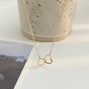 Elegant gold double interlocking heart necklace on a minimalist ceramic setup