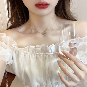 Close-up of a delicate silver bow necklace with a zircon pendant on a female model