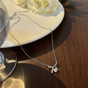 Detail of silver bow necklace with heart zircon on a rustic wooden table with white rose