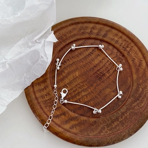 Macro detail of S925 sterling silver beaded bracelet with lobster clasp on wooden tray