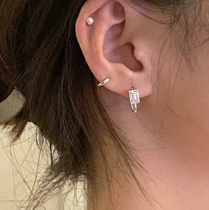 Close-up of S925 silver hoop earrings and rectangular zircon crystal on a female ear