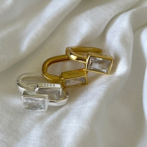 Macro view of S925 silver geometric hoop earrings with emerald-cut zircon on linen