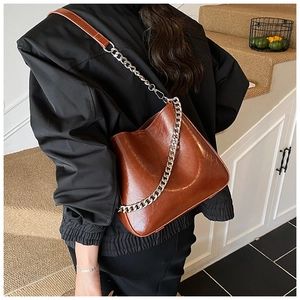 Detail of a brown glossy leather bucket bag featuring a thick silver decorative chain