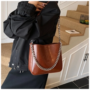 Detail view of a brown glossy leather bucket bag with chunky silver chain and strap
