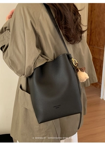 Detail of black pebbled leather bucket bag with khaki plush bear charm on model