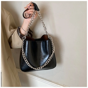 Detail of glossy black bucket bag featuring a thick silver metal chain and thin strap
