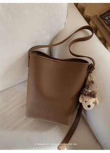 Detail of brown lychee grain bucket bag with a cute plush bear charm on white sofa