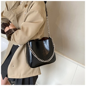 Detail of glossy black oil-wax leather bucket bag with chunky silver chain strap
