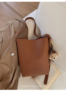 Brown lychee leather bucket bag with plush bear charm on a cozy beige sofa background