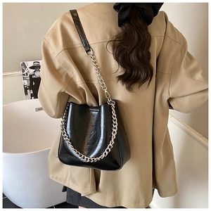 Detail of black glossy leather bucket bag with chunky metal chain and shoulder strap