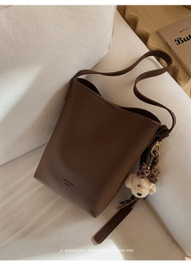 Close-up of dark brown lychee texture leather bucket bag with cute bear charm detail