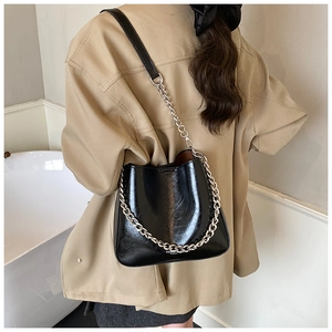Detailed view of glossy black leather bucket bag with silver chain strap on model