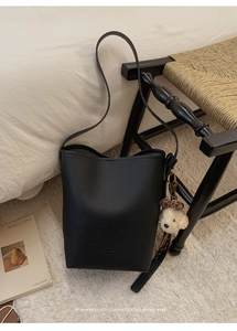 Macro detail of black litchi texture leather bucket bag with a cute brown bear charm