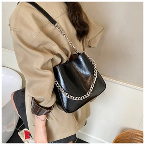 Detail of black glossy handbag with silver chain and leather strap on trench coat model