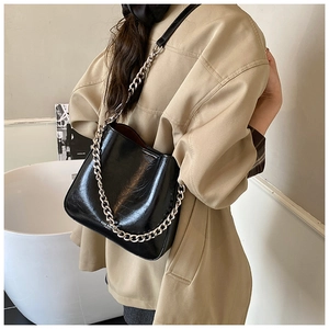 Detail of black glossy bucket bag featuring chunky silver metal chain strap for women