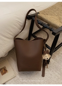 Detailed texture of brown litchi grain leather bucket bag with cute plush bear charm