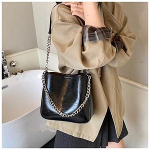 Detail of a black glossy leather bucket bag featuring a thick silver metal chain shoulder strap