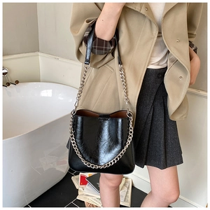 Detail of glossy pleated leather bucket bag with chain strap styled with a trench coat
