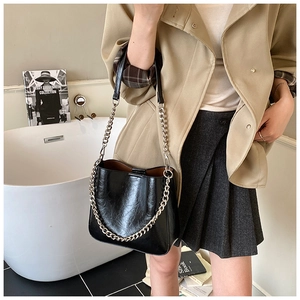 Close-up of black glossy leather bucket bag with silver chain and leather strap