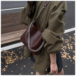 Detail of dark brown glossy leather crossbody bag with silver chain and leather strap