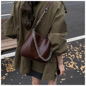 Detail of dark brown glossy leather tote bag with thick silver chain on park bench