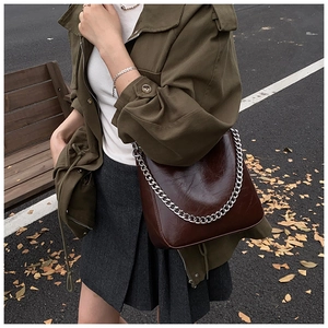Detail of dark brown glossy leather handbag with silver chunky metal chain in street setting