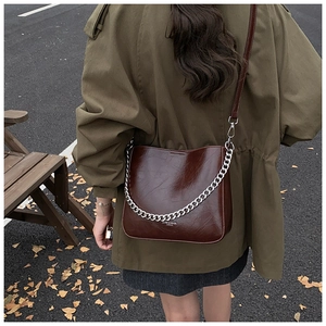 Outdoor street view of a large brown bucket bag with silver chain and leather strap