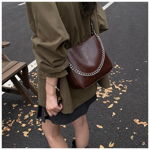 Detailed close-up of dark brown leather shoulder bag with a thick silver metal chain strap