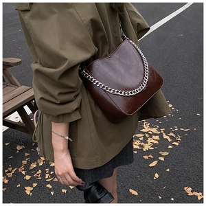 Detail of a dark brown oil-wax leather shoulder bag featuring a chunky silver chain strap