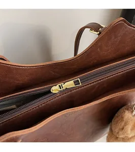 Detailed close-up of premium golden metal zipper on a vintage brown tote bag with plush charm