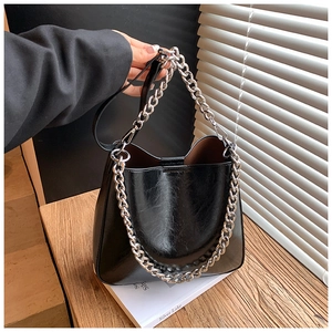 Detail of glossy black leather bucket bag with chunky silver chain and smooth finish