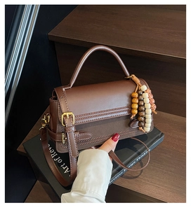 Detail of vintage brown leather handbag with wooden bead charm and elegant handle