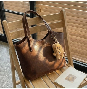 Detail of vintage brown leather tote bag with teddy bear pendant in natural sunlight