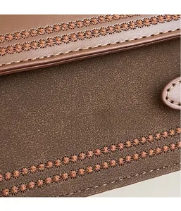 Macro shot of dark brown frosted fabric with vintage floral embroidery and leather stitching