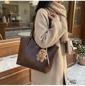 Detail of dark brown leather tote bag with gold logo and plush puppy charm in winter setting
