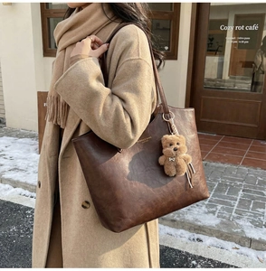Detail of vintage brown tote bag featuring golden lettering and a plush bear charm accessory