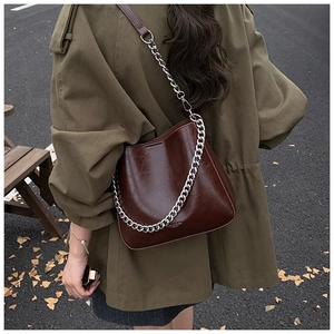 Close-up of a large brown wax leather bucket bag with silver chain in an outdoor street setting