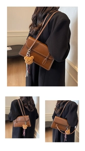 Dettaglio borsa baguette vintage in pelle cerata con ciondolo orso e cuciture bianche
