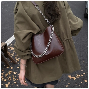 Close-up of brown faux leather bucket bag with silver chain and logo in autumn setting