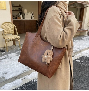 Detailed view of a vintage brown tote bag with a plush bear charm in a winter setting