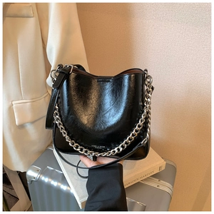 Detail of glossy black leather handbag with chunky silver chain and long shoulder strap