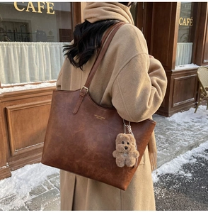 Detail of vintage brown tote bag with plush bear charm and faux leather texture