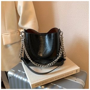 Detail of black glossy leather bucket bag with silver chain on a stack of white books
